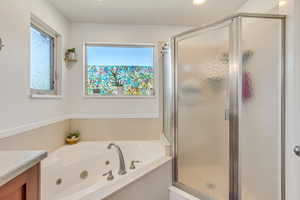 Bathroom featuring a corner jetted soaking tub with deck-mounted fixtures, an enclosed shower with obscured glass, and dual windows