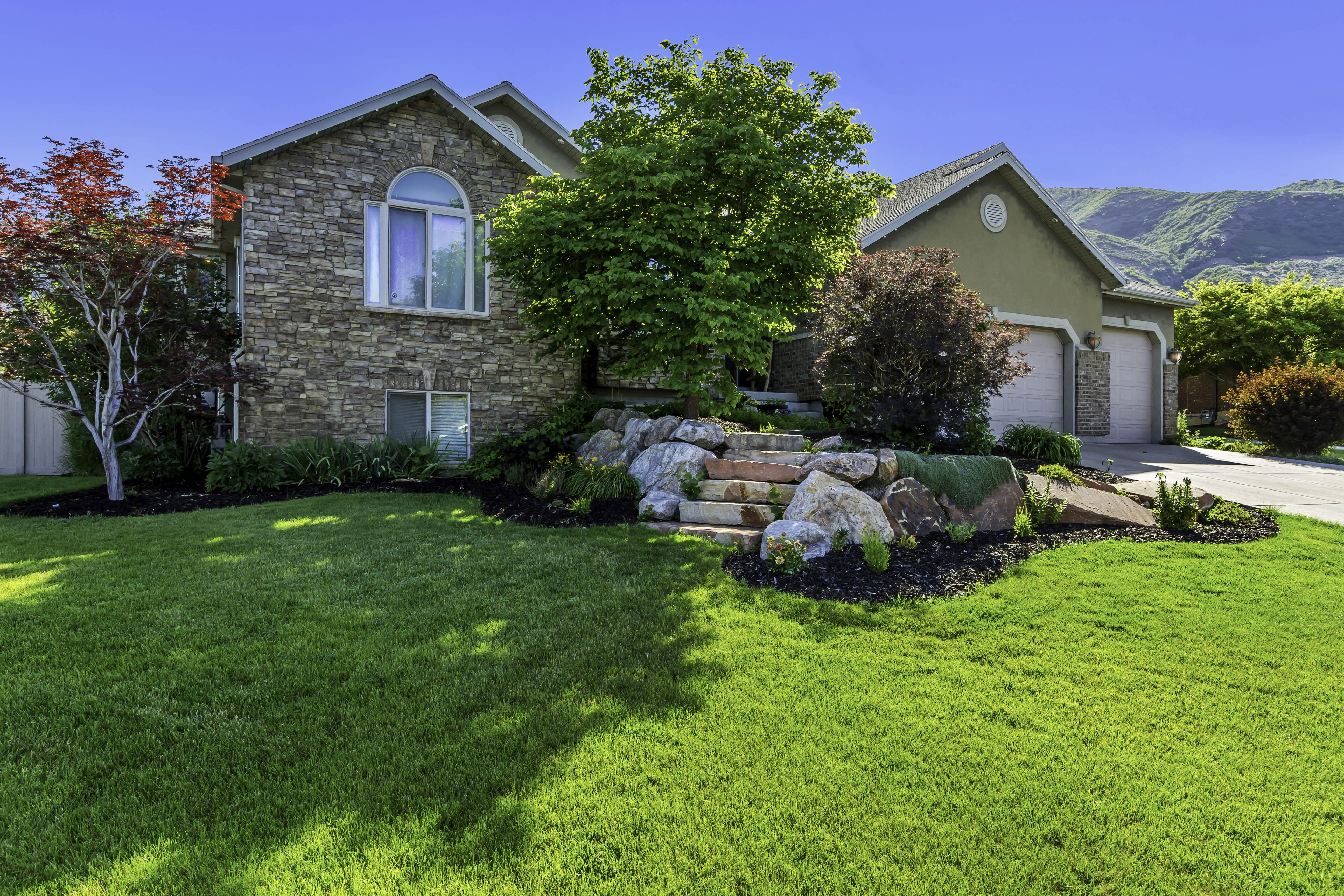 Stone facade residence featuring an arched window and an attached multi-car garage with stone accents