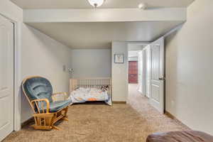 Carpeted room with white walls, featuring a white paneled door, recessed ceiling light, and a second doorway revealing a hallway with additional white doors
