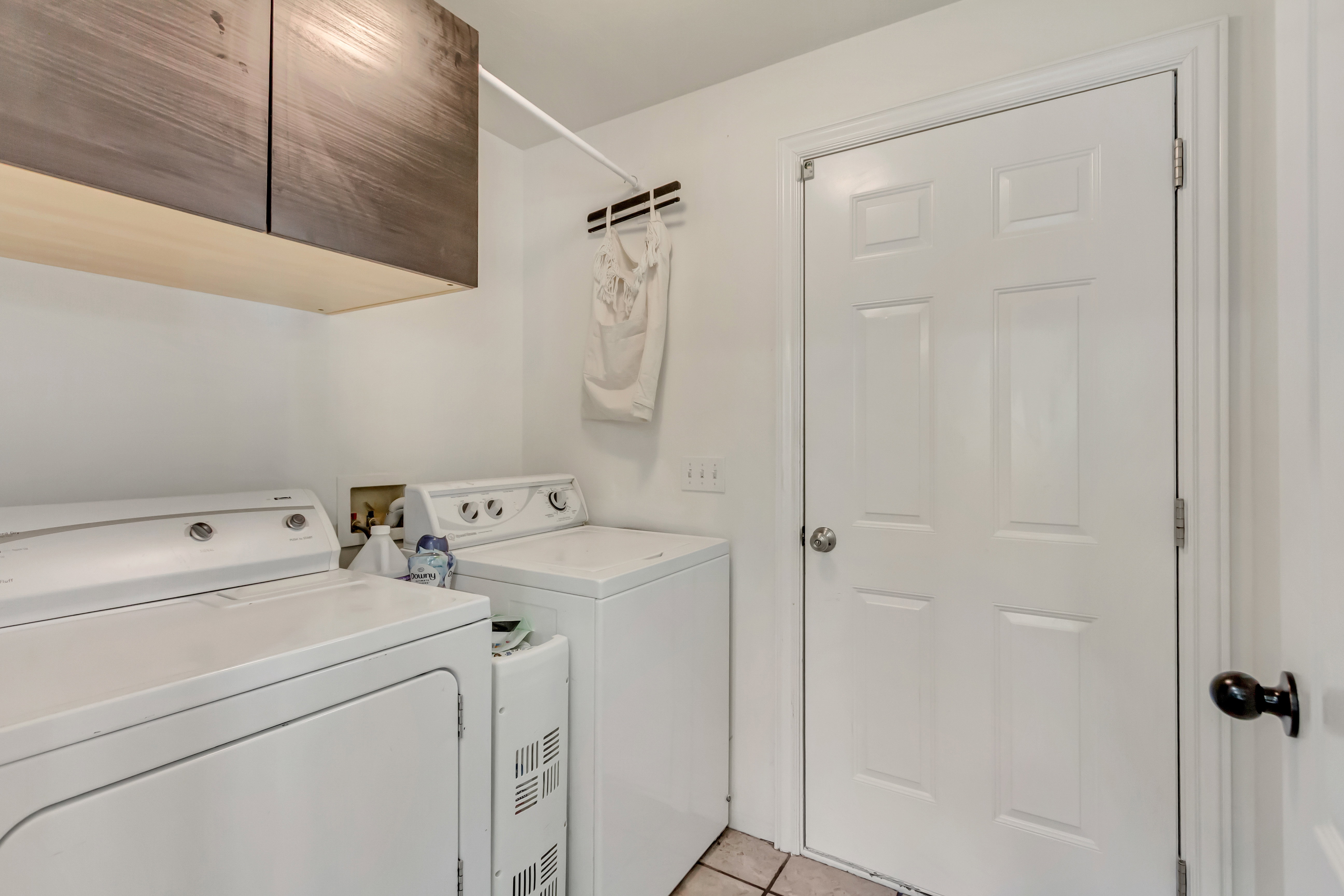 Laundry area featuring wood-finish upper cabinetry, a white panel door, and tile flooring