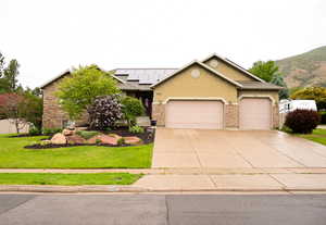 Exterior with a two-car garage, stone and stucco facade, solar panels, and mature landscaping