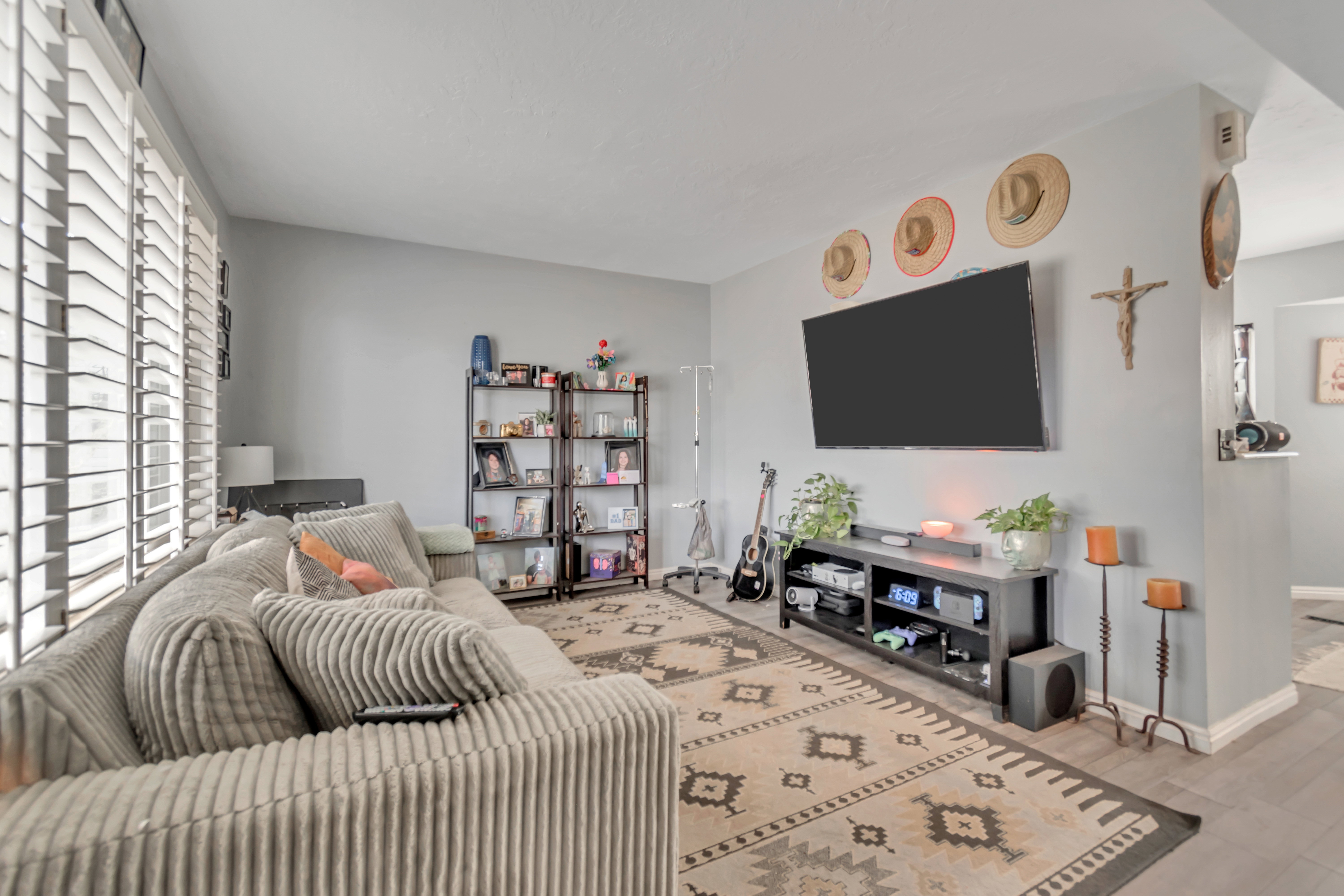 Spacious living area featuring light gray walls, wood-finish flooring, and white louvered window treatments