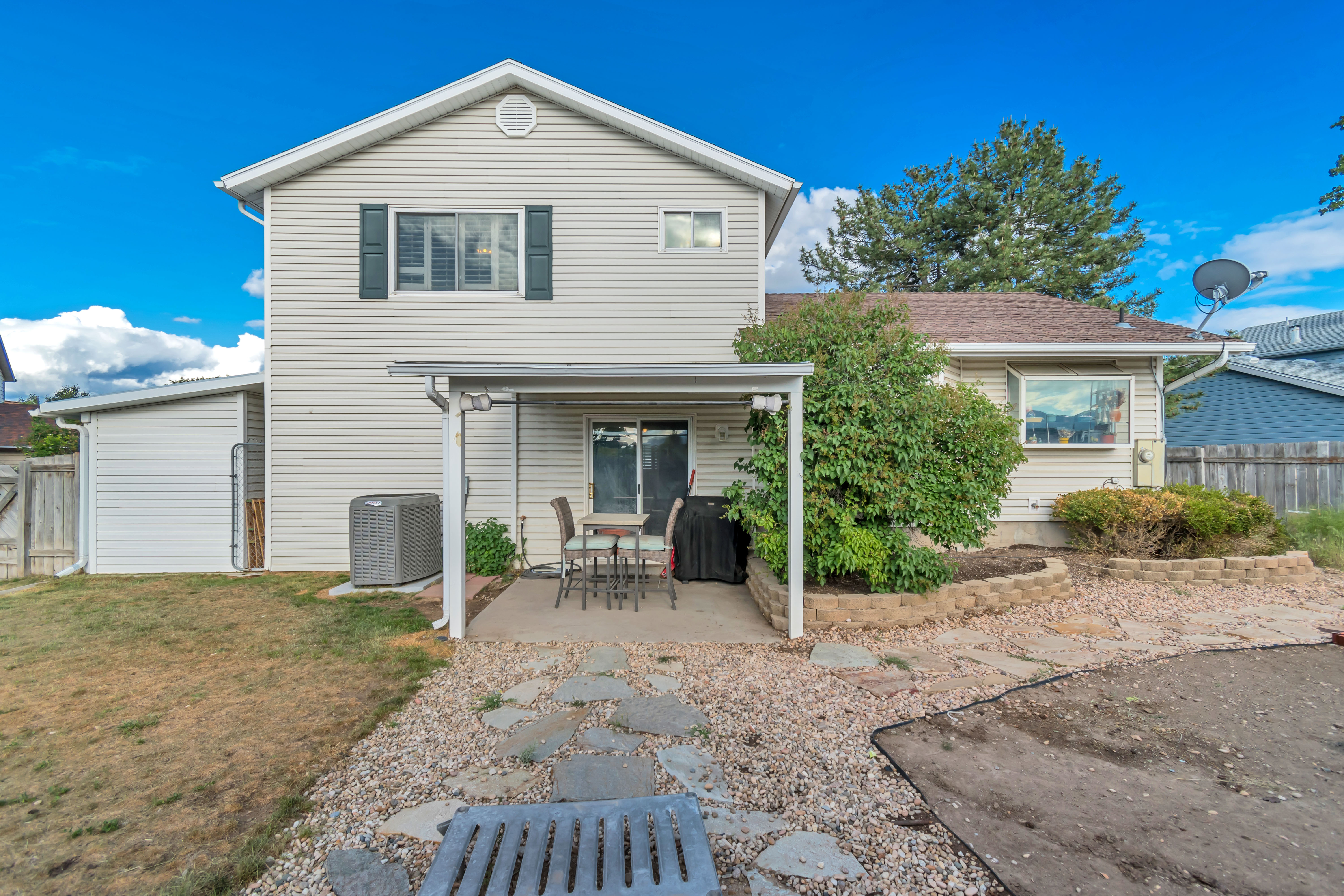 Rear exterior with a covered patio, sliding glass door, and an extended gravel area