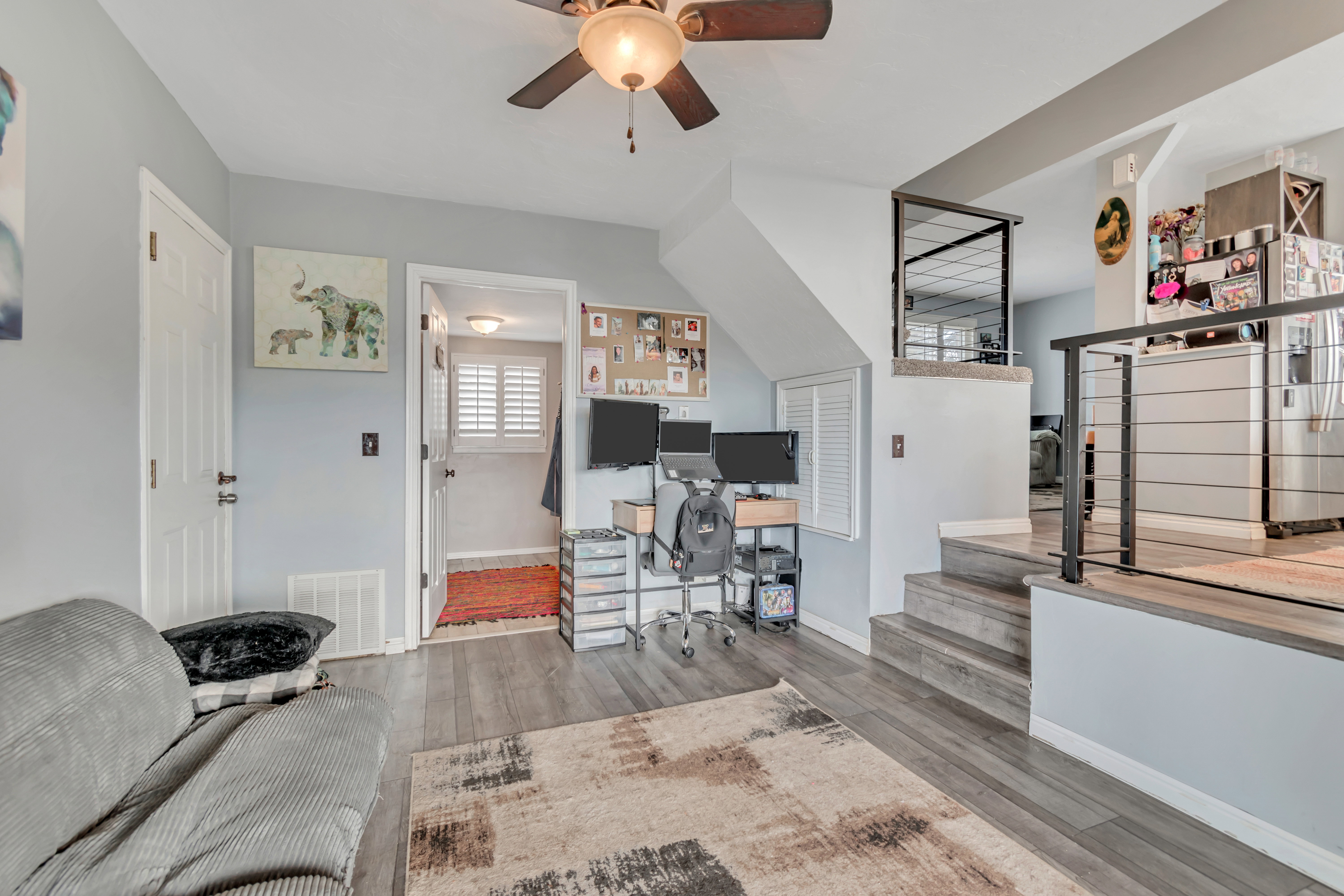 Split-level interior featuring wood-finish flooring, a ceiling fan with integrated lighting, and a contemporary metal railing