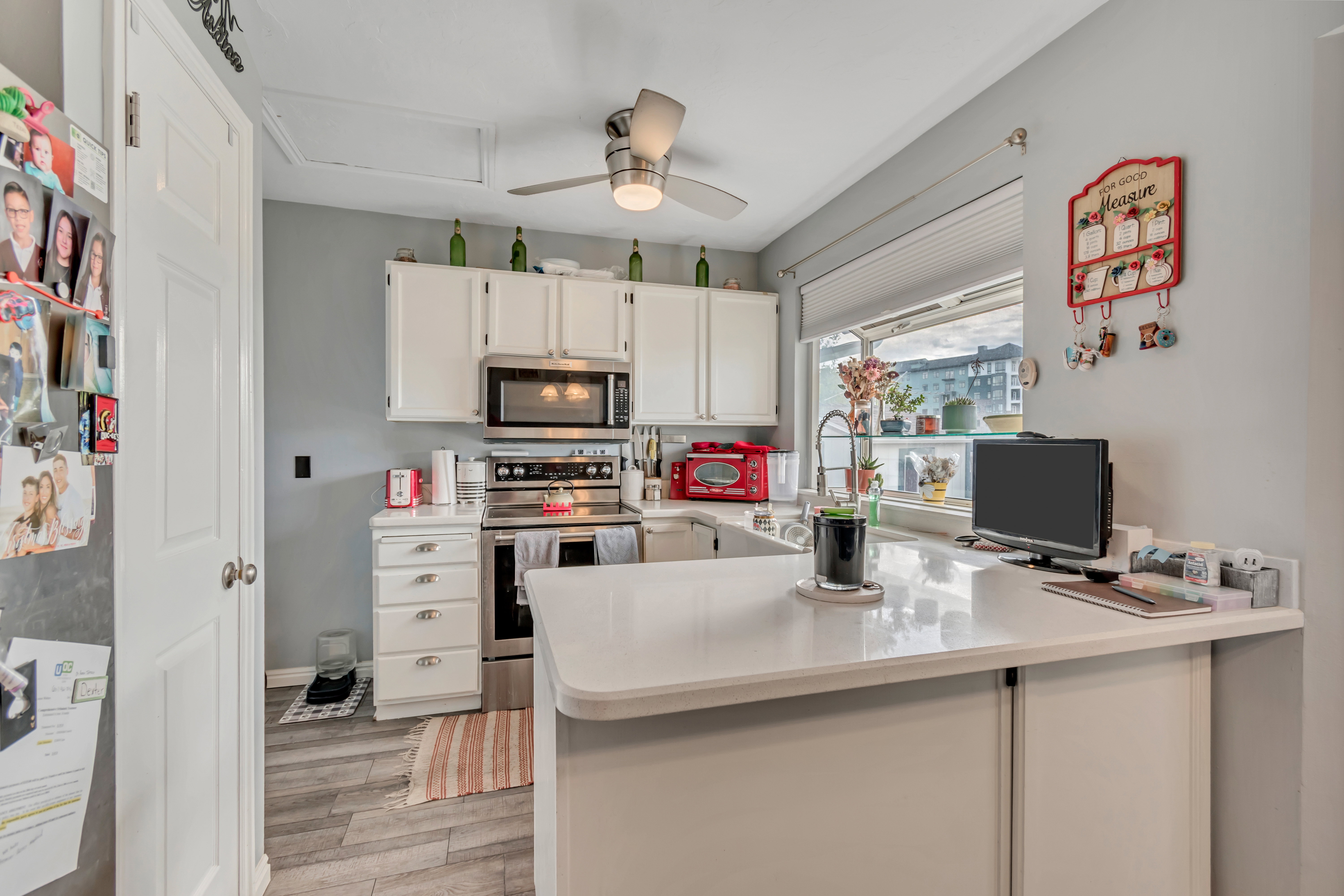 Kitchen featuring white cabinetry, stainless steel appliances, a window above the sink, light-colored countertops, and wood-finish flooring