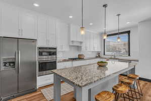 Kitchen featuring a large central island with a stone countertop, white shaker cabinetry, stainless steel appliances, subway tile backsplash, and wood-finish flooring
