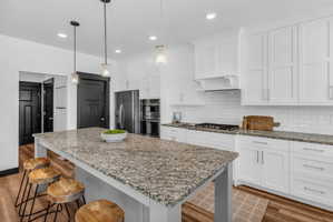 Kitchen featuring a large island with a stone countertop, white shaker cabinetry, stainless steel appliances, and wood-finish flooring