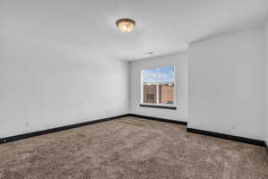 Carpeted room featuring a single window with blinds, white walls, dark baseboards, and a ceiling-mounted light fixture