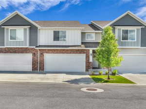 Modern townhome exterior featuring a combination of brick and siding, multiple attached garages, concrete driveways, and a manicured lawn with mature trees