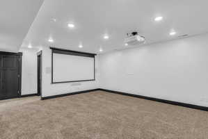 Dedicated media room featuring a large projection screen, ceiling-mounted projector, recessed lighting, and integrated wall speakers