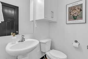 Pedestal sink with chrome faucet, white toilet, and upper cabinetry