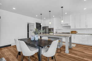 Spacious open-concept kitchen and dining area featuring wood-finish flooring, white shaker cabinetry, an island with seating, a subway tile backsplash, and recessed and pendant lighting