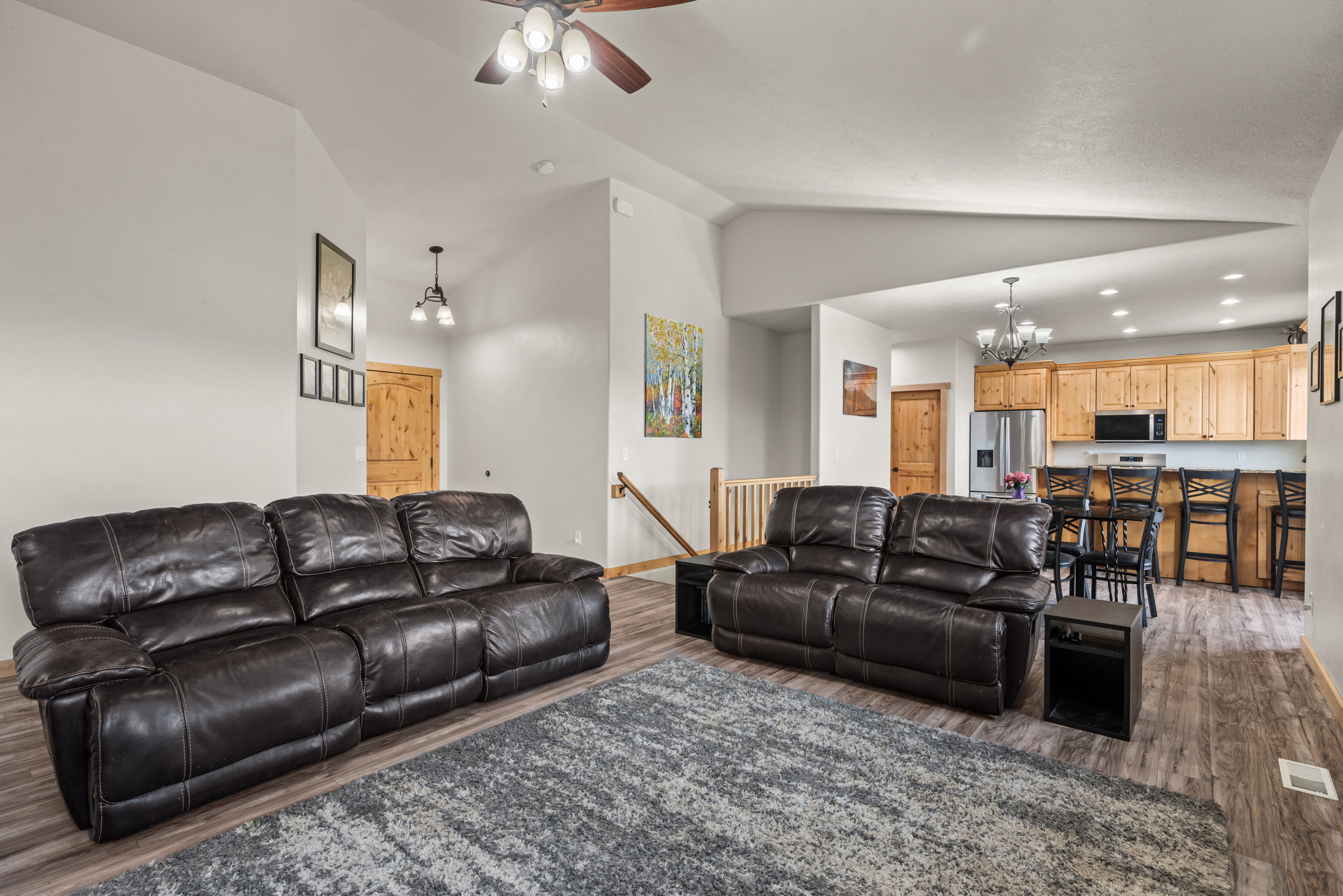 Open-concept living area featuring vaulted ceilings, wood-finish flooring, and a ceiling fan with integrated lighting