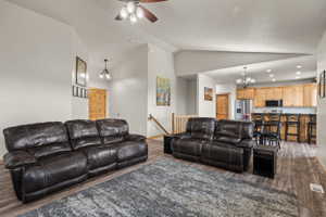 Open-concept living area featuring vaulted ceilings, wood-finish flooring, and a ceiling fan with integrated lighting