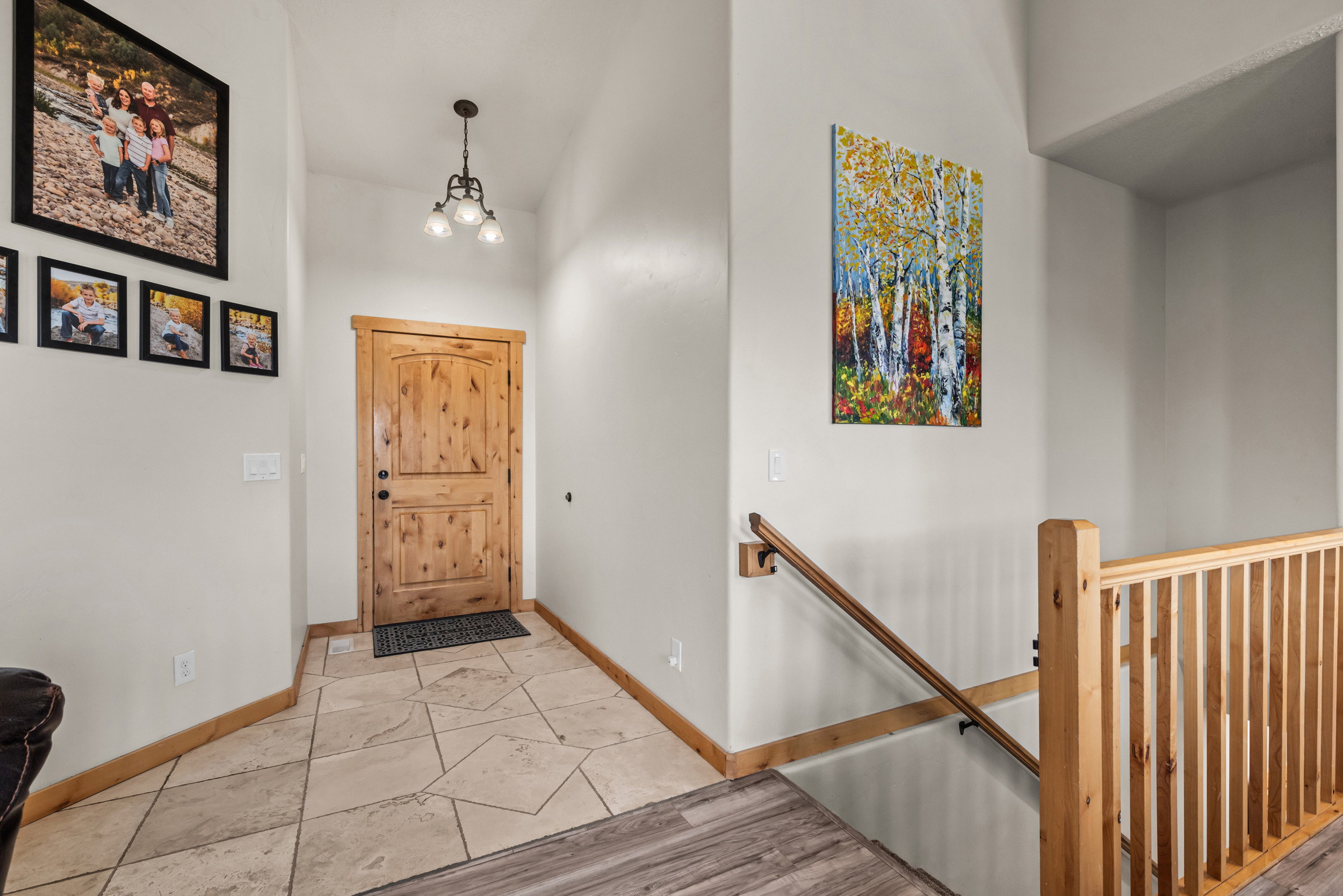 Entryway featuring a natural wood door with dark hardware, a three-light chandelier, and light-toned tile flooring