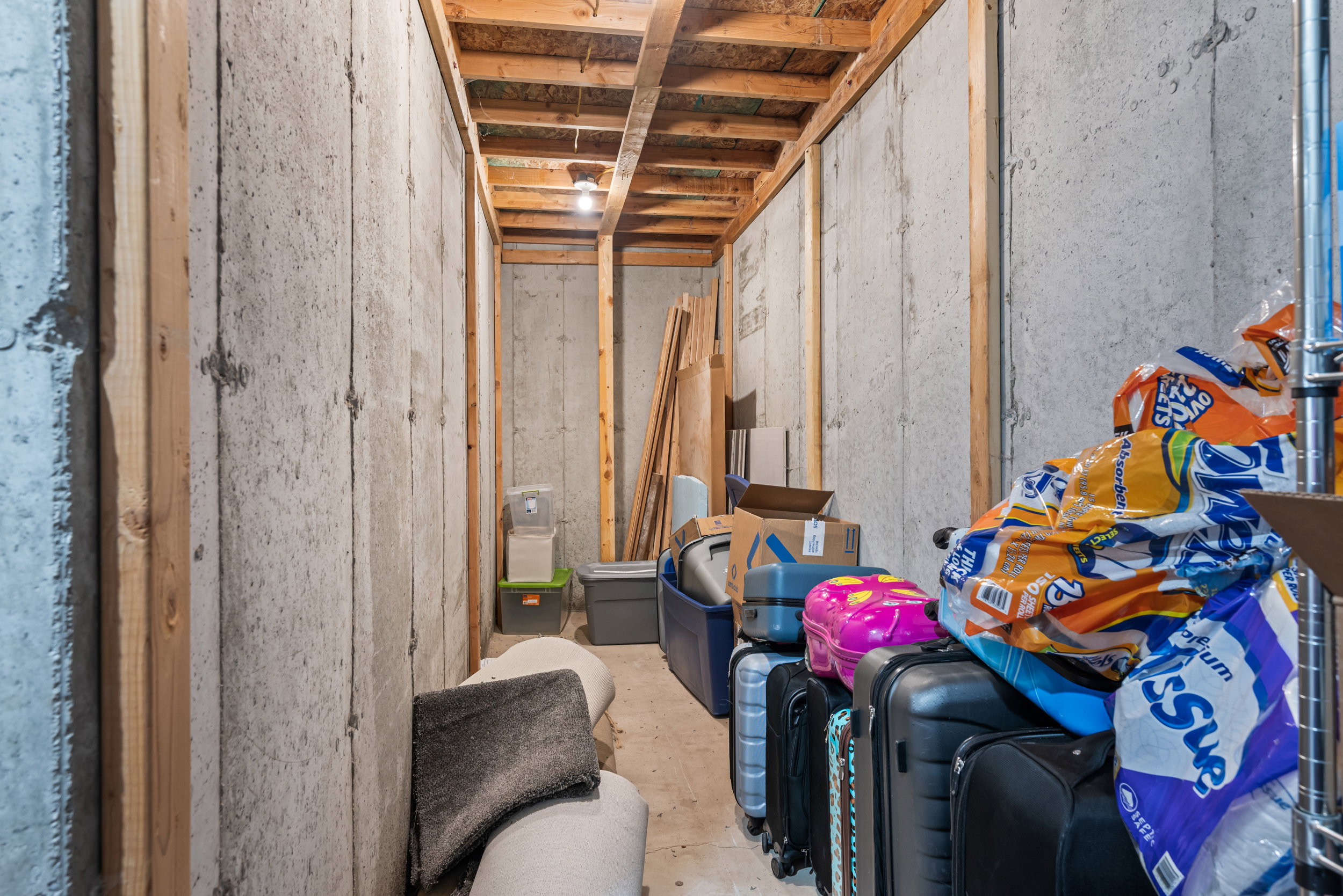 Unfinished basement area featuring exposed wood framing, concrete foundation walls, and overhead lighting