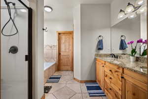 Bathroom featuring a wood-finish vanity with a light-colored countertop, a built-in shower with dark bronze hardware, a built-in bathtub with a tiled surround, a full-width mirror, and large format floor tiles