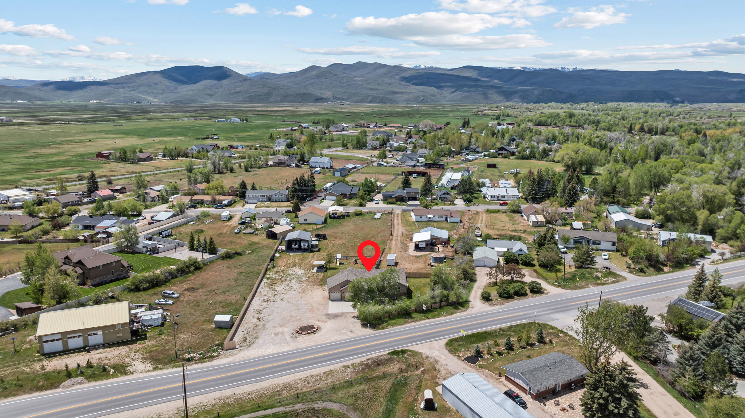 Expansive lot with a single-story residence and detached garage, featuring a paved driveway and surrounding natural landscape