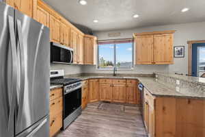 Kitchen featuring light wood cabinetry, granite countertops, stainless steel appliances, wood-finish flooring, and recessed lighting