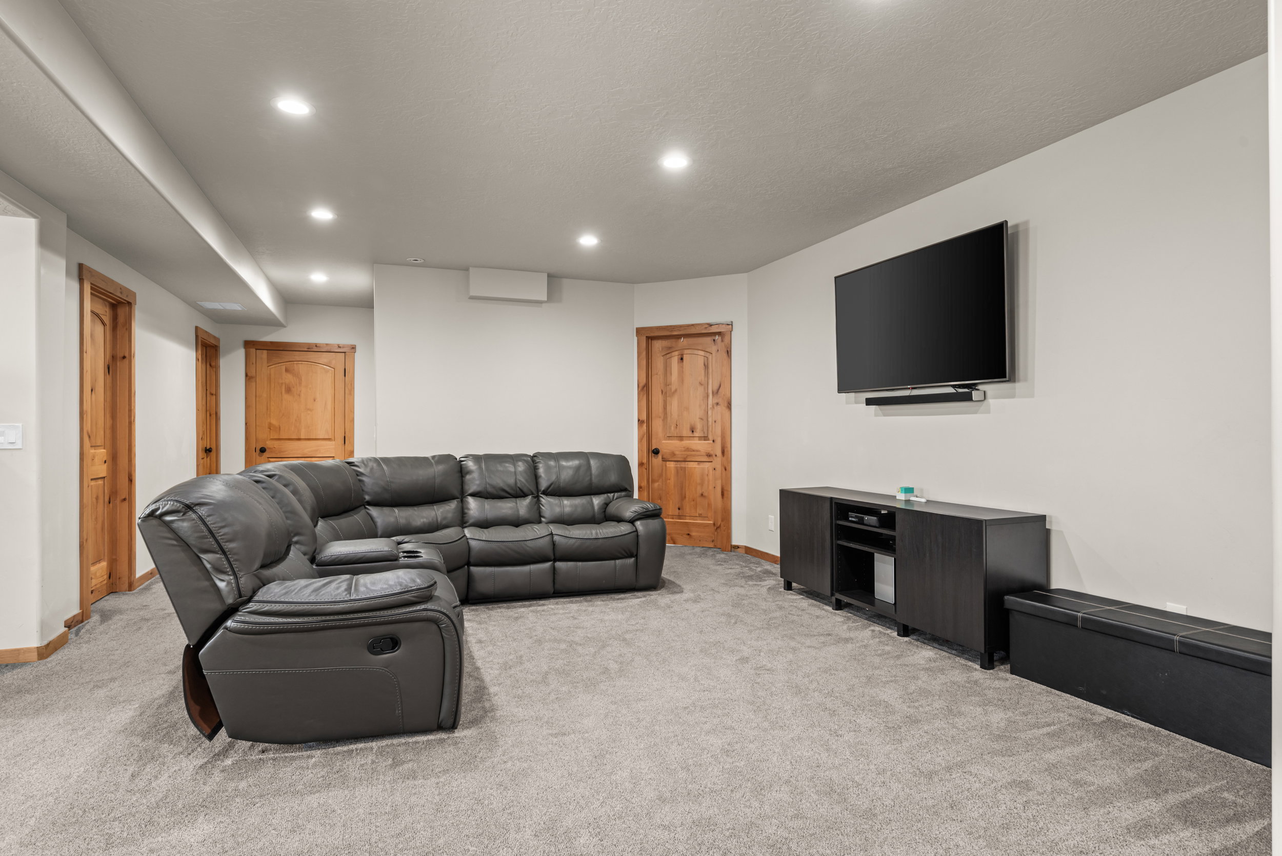 Recessed lighting illuminates a spacious room featuring light gray carpeting and white walls