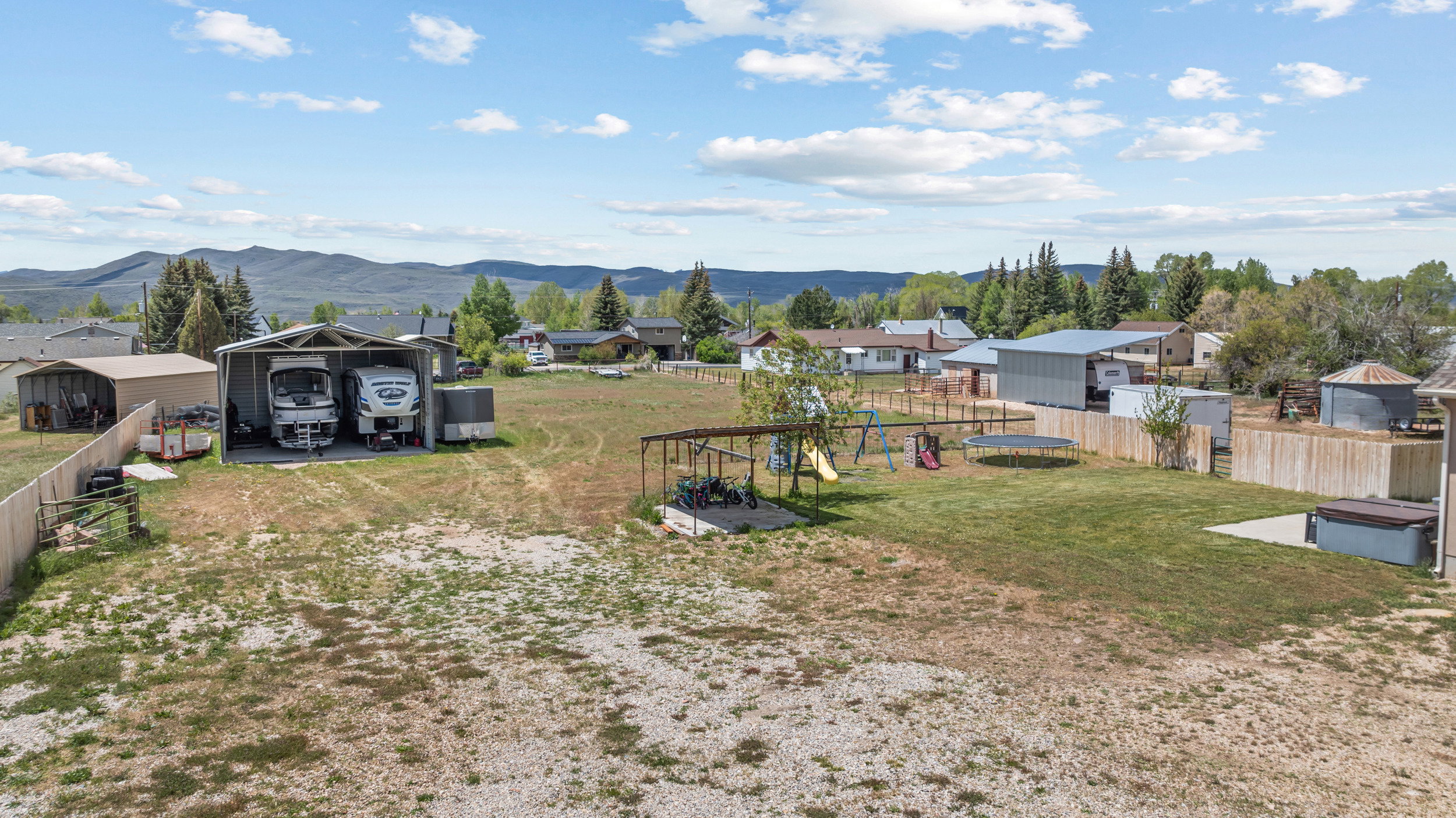 Expansive property featuring a large metal carport, a separate shed, a fenced perimeter, a concrete patio, and a hot tub