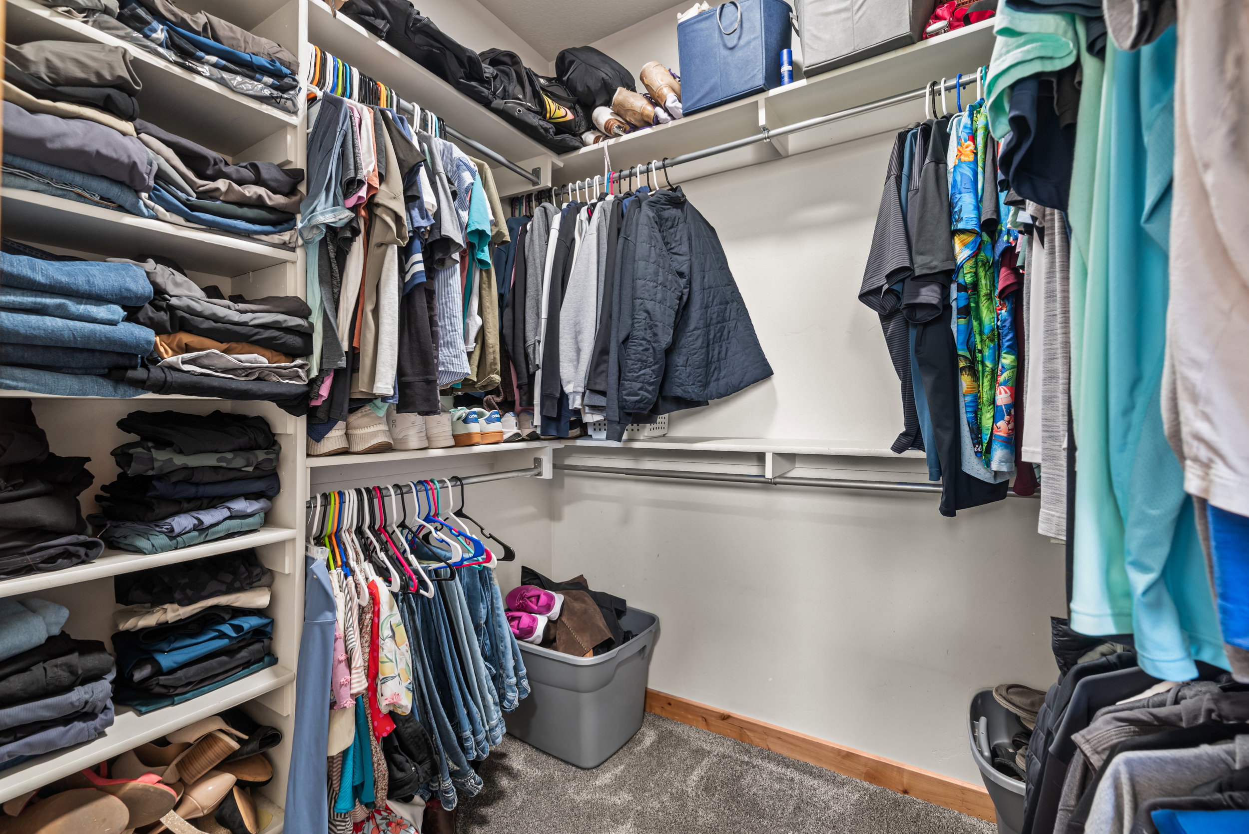 Walk-in closet featuring built-in shelving, multiple hanging rods, and wood-finish base trim