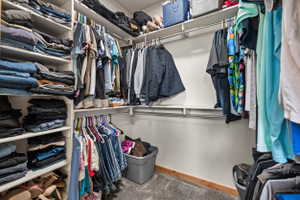 Walk-in closet featuring built-in shelving, multiple hanging rods, and wood-finish base trim