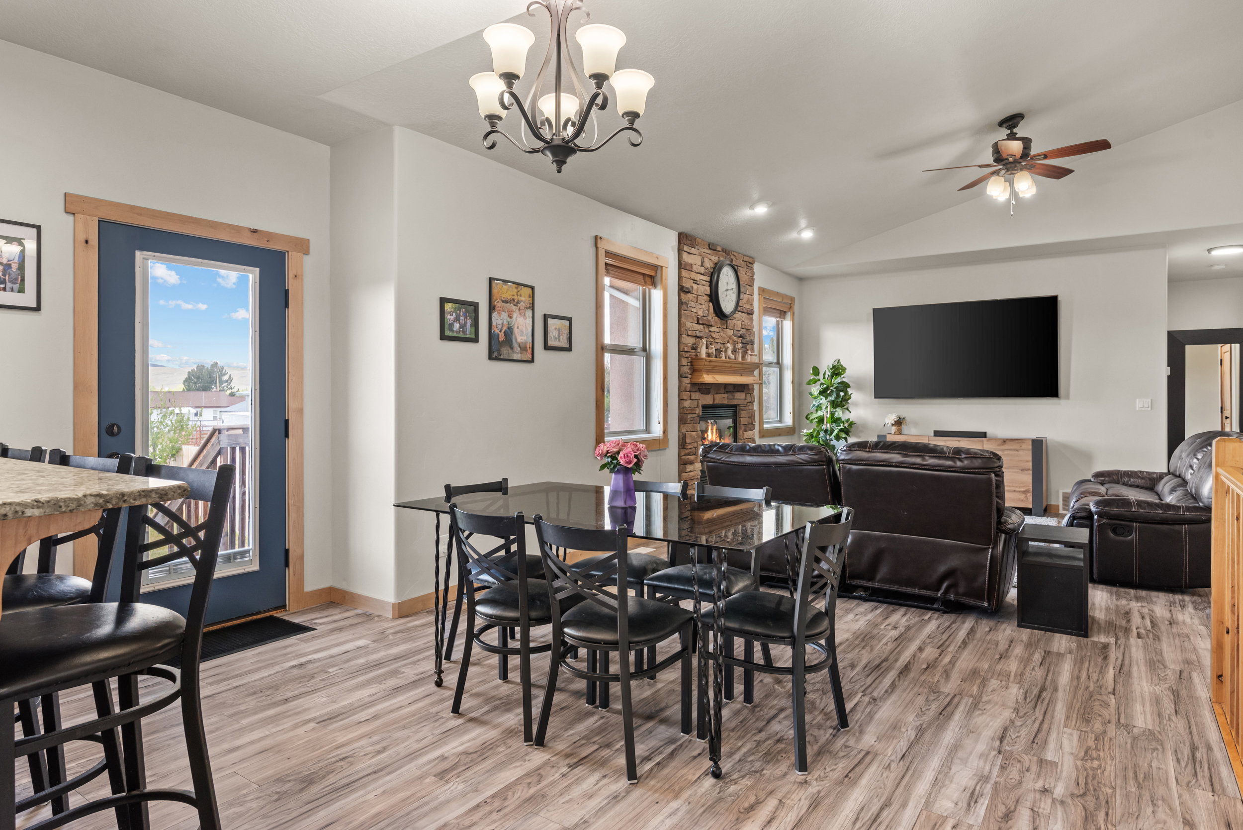 Open-concept living area featuring wood-finish flooring, a stone-faced fireplace, a vaulted ceiling, and recessed lighting