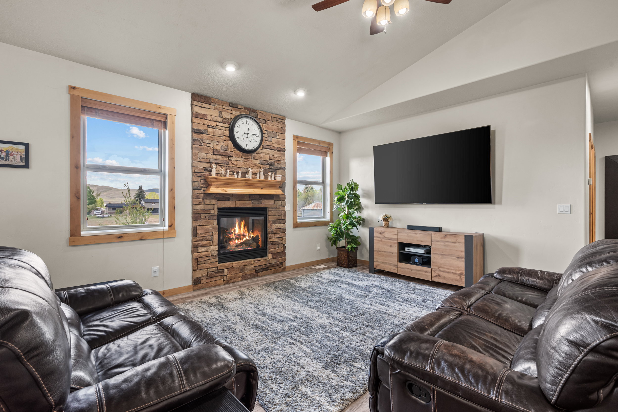 Living room featuring a stone-clad fireplace with a wood mantle, vaulted ceilings, recessed lighting, and wood-finish flooring