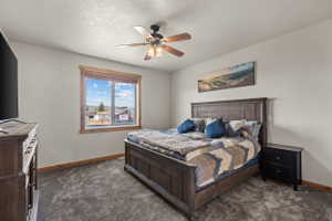 Carpeted bedroom featuring a large window with natural wood trim, a ceiling fan with light fixture, and neutral wall paint