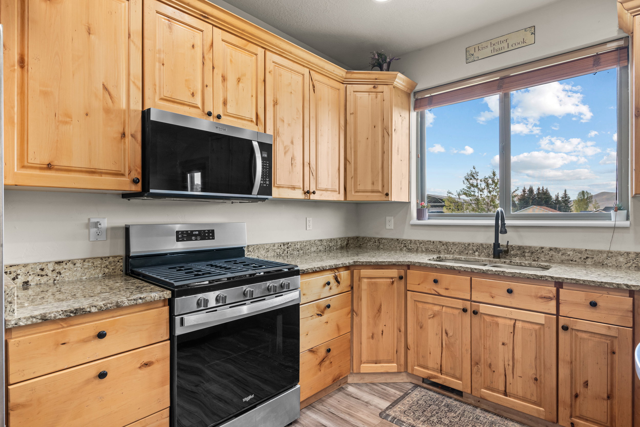 L-shaped kitchen with light wood cabinetry, granite countertops, and wood-finish flooring