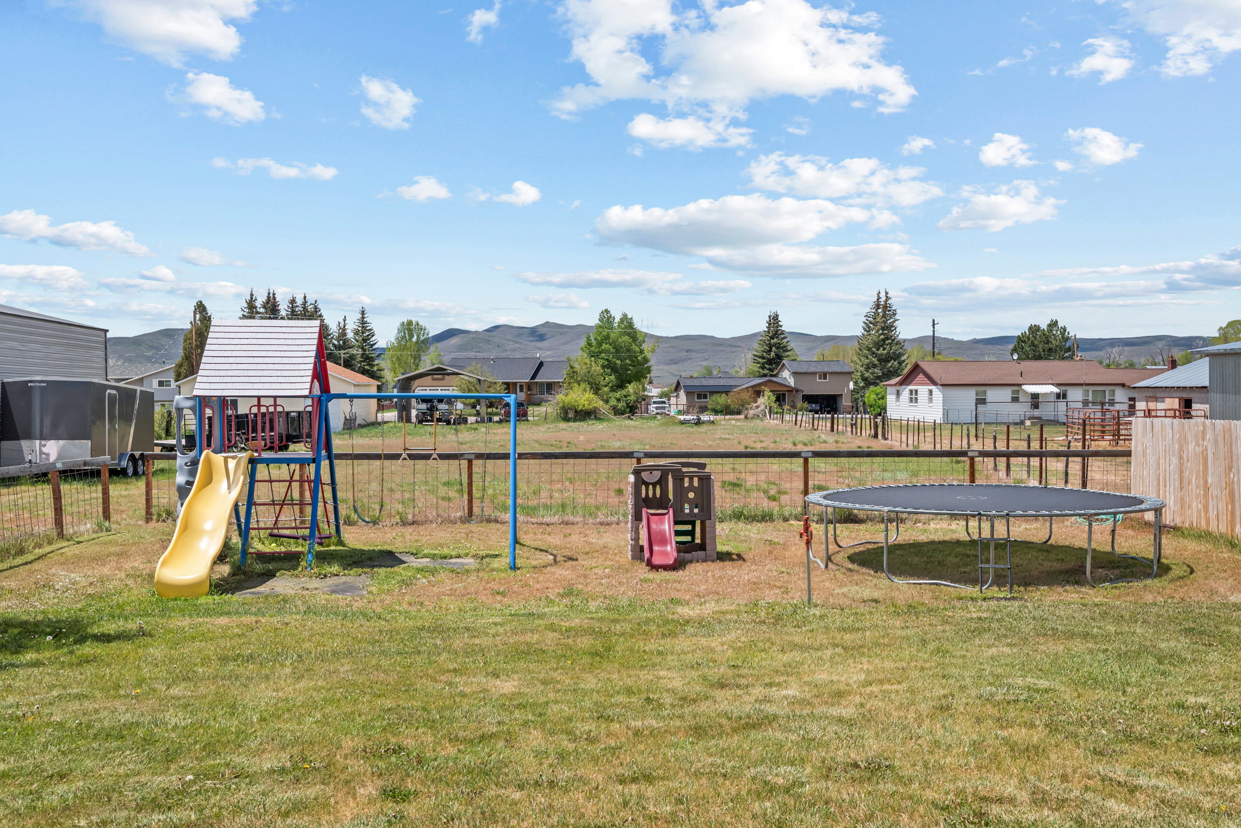 Expansive outdoor area featuring a full-size trampoline, a wooden playset with slide, and a swing set
