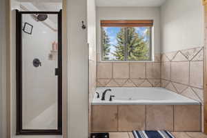 Spacious bathroom featuring a corner soaking tub with tile surround, an adjacent shower with a dark-framed glass enclosure, and a window with natural light