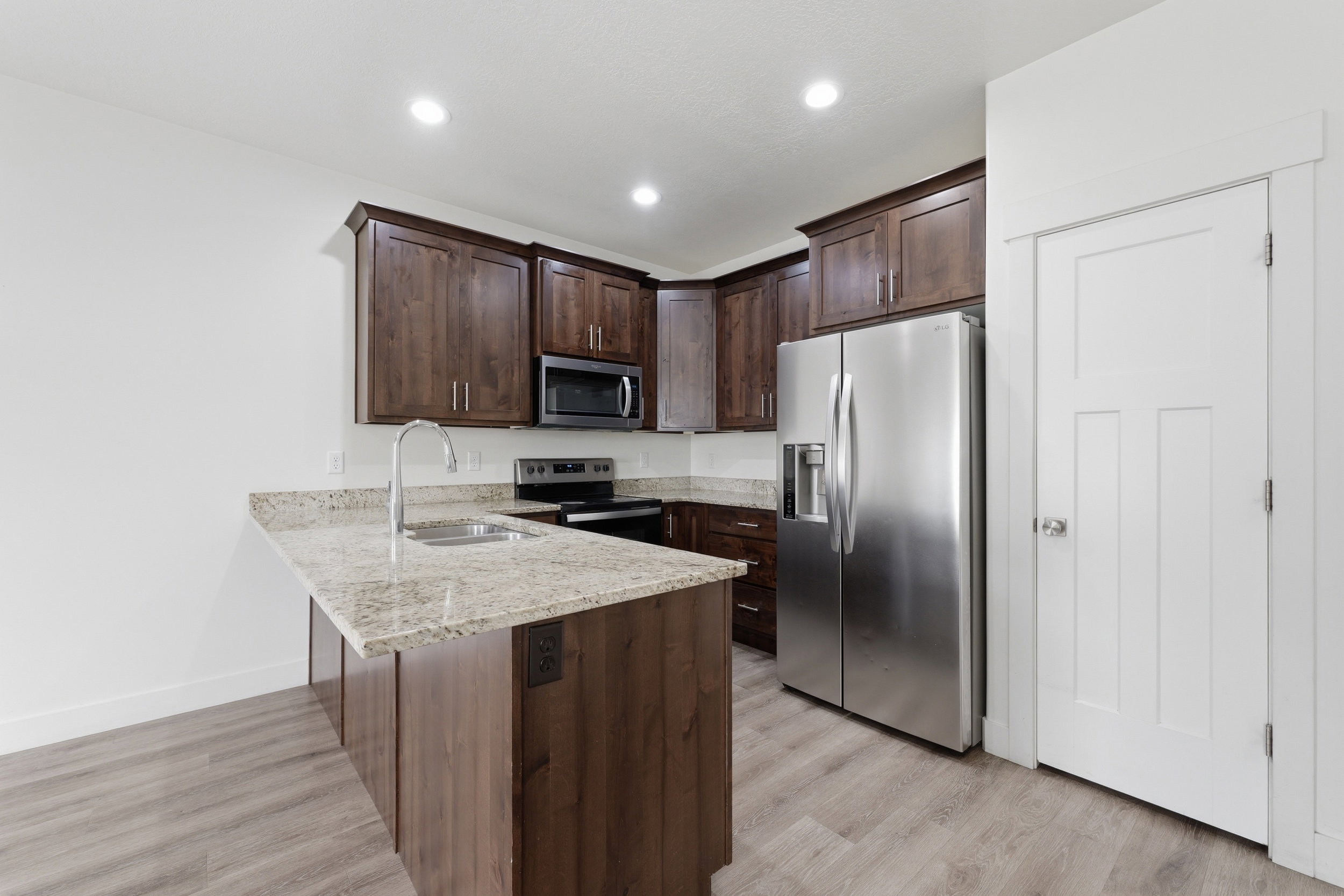 Kitchen featuring wood-finish cabinetry, light-toned granite countertops, and stainless steel appliances including a side-by-side refrigerator, microwave, and range