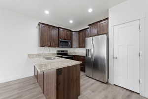 Kitchen featuring wood-finish cabinetry, light-toned granite countertops, and stainless steel appliances including a side-by-side refrigerator, microwave, and range