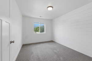 Bedroom featuring a shiplap accent wall, neutral carpeting, and a window providing natural light