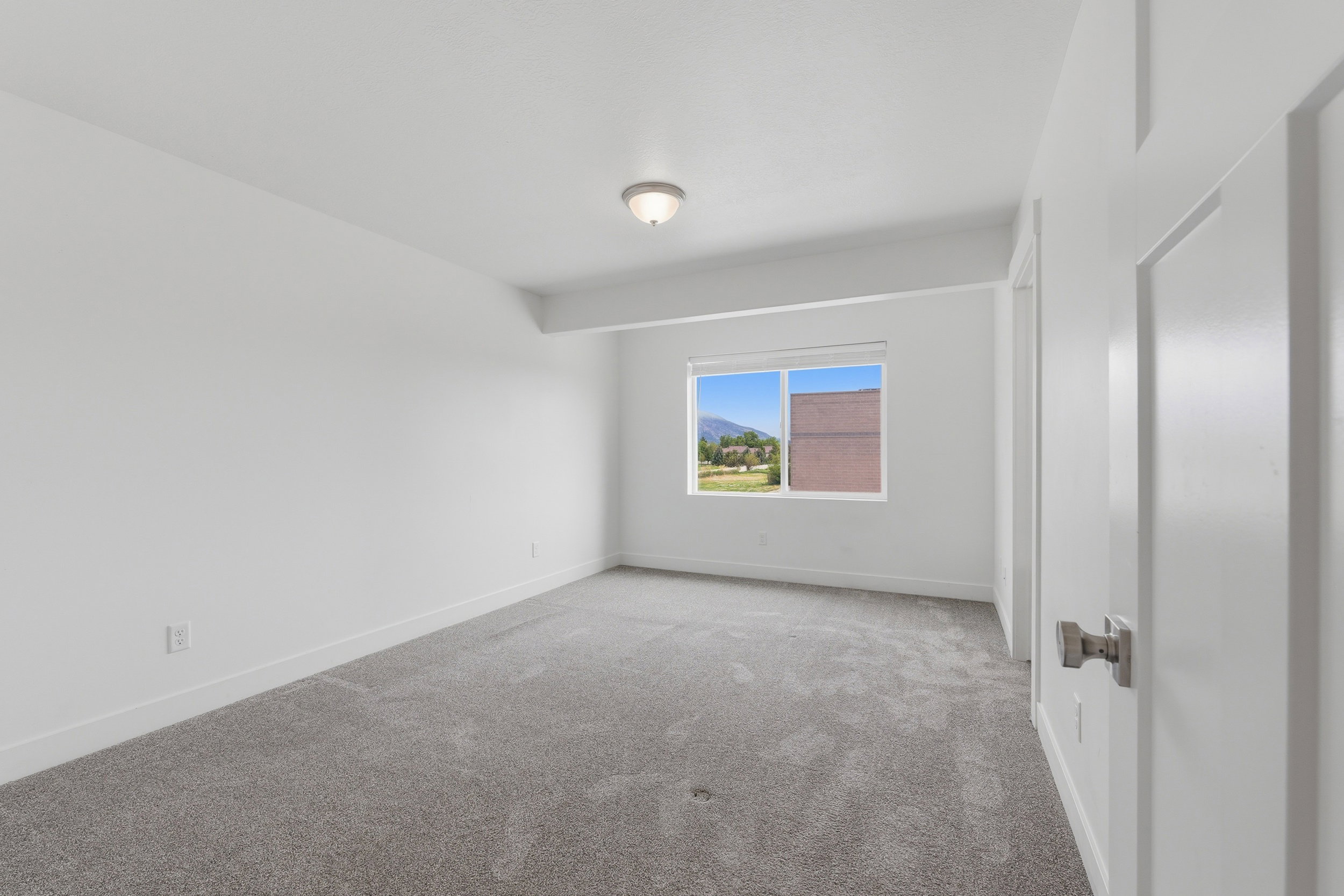 Spacious room with plush gray carpeting, white walls, and a large window offering natural light
