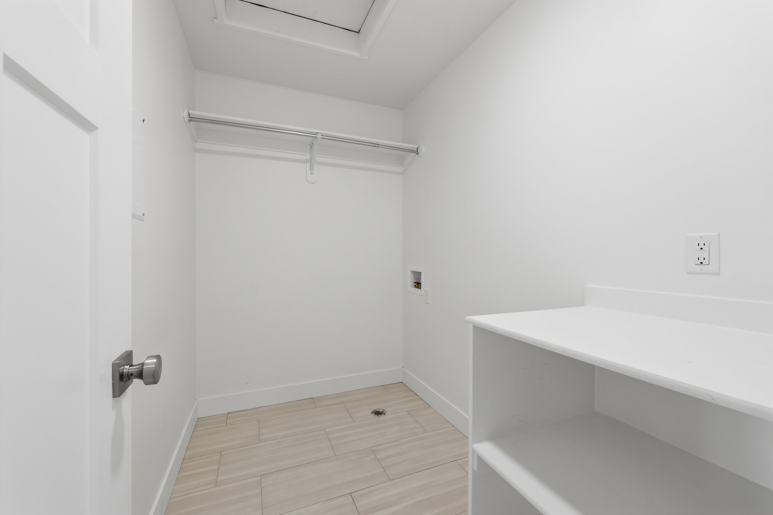 Bright utility space featuring light-toned wood-finish flooring, white walls, and built-in shelving
