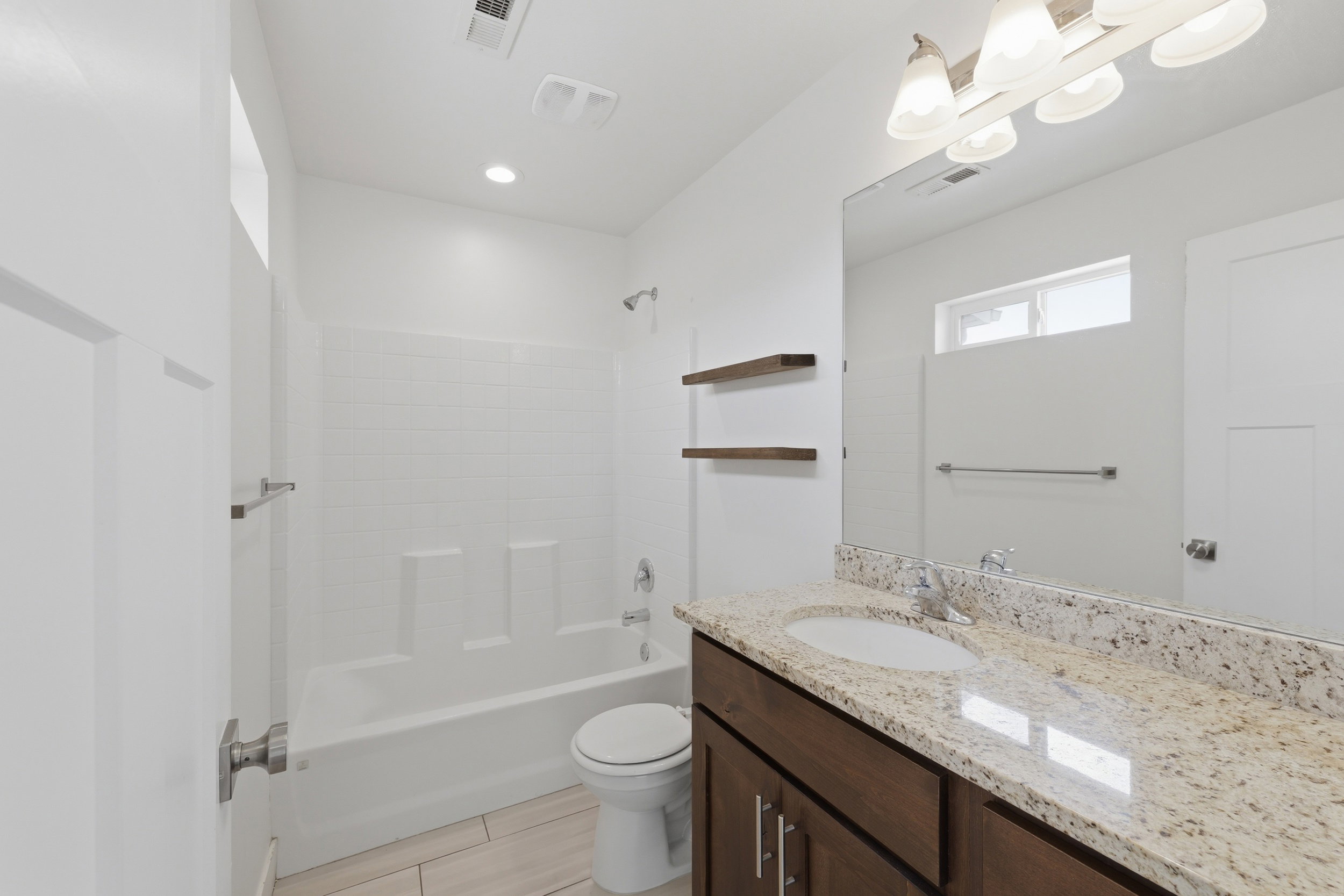 Bathroom featuring a vanity with a light granite countertop and undermount sink, dark wood-finish cabinetry, a full-width mirror, and a shower-tub combination with white subway tile surround