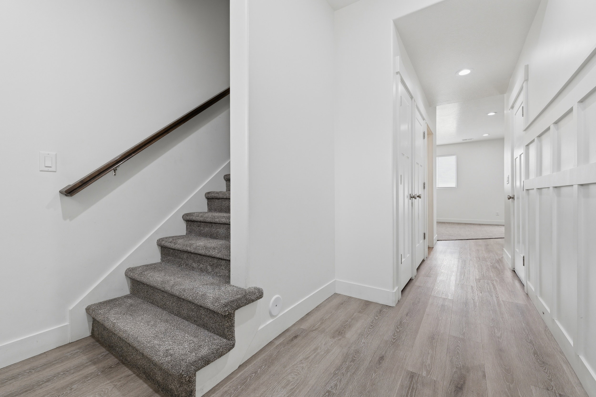 Staircase with gray carpeted treads and a dark wood handrail, complemented by light wood-finish flooring