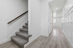 Staircase with gray carpeted treads and a dark wood handrail, complemented by light wood-finish flooring