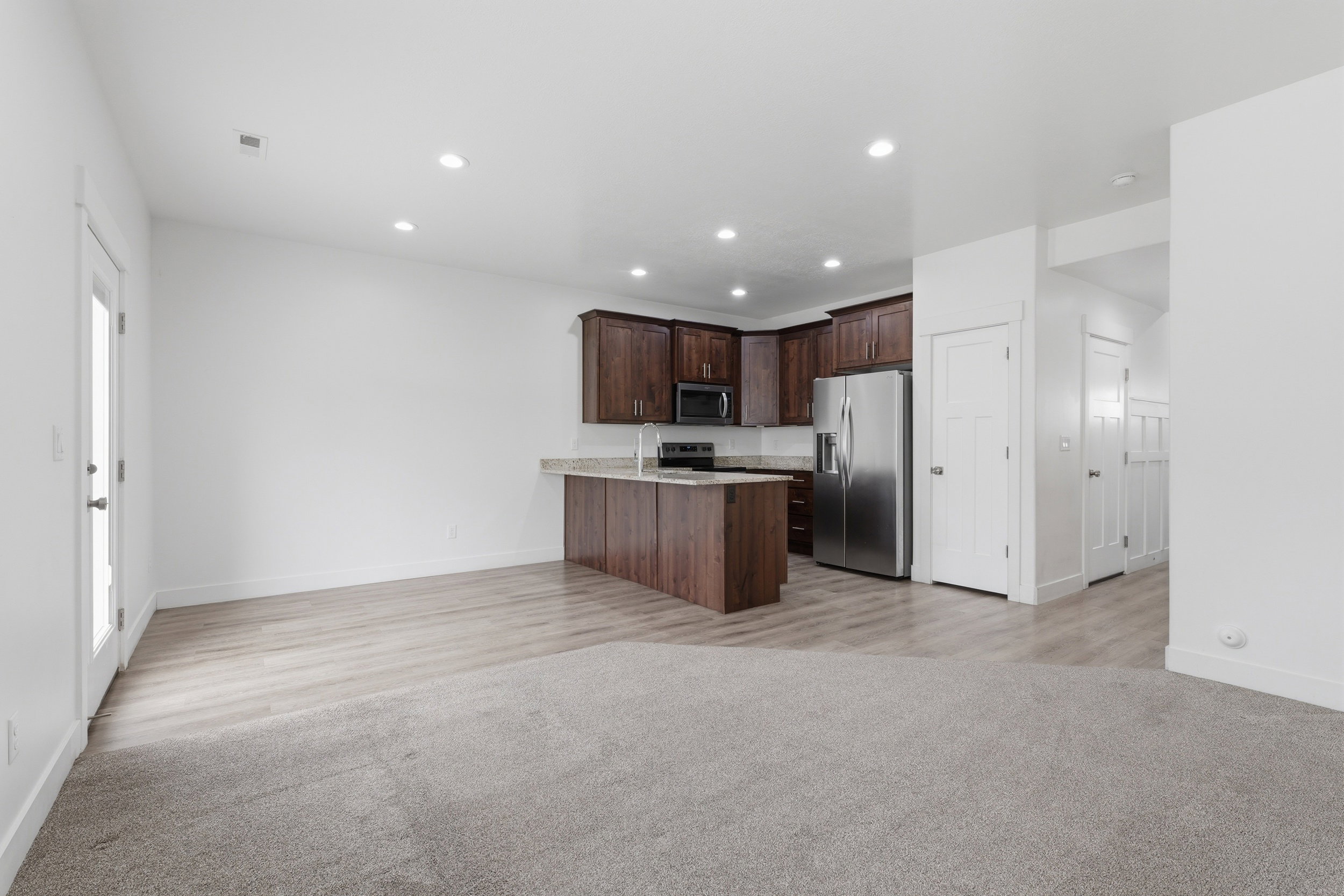 Open-concept living area featuring a kitchen with dark wood-finish cabinetry, stainless steel appliances, and a peninsula with a light-toned countertop