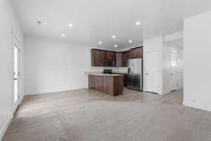Open-concept living area featuring a kitchen with dark wood-finish cabinetry, stainless steel appliances, and a peninsula with a light-toned countertop