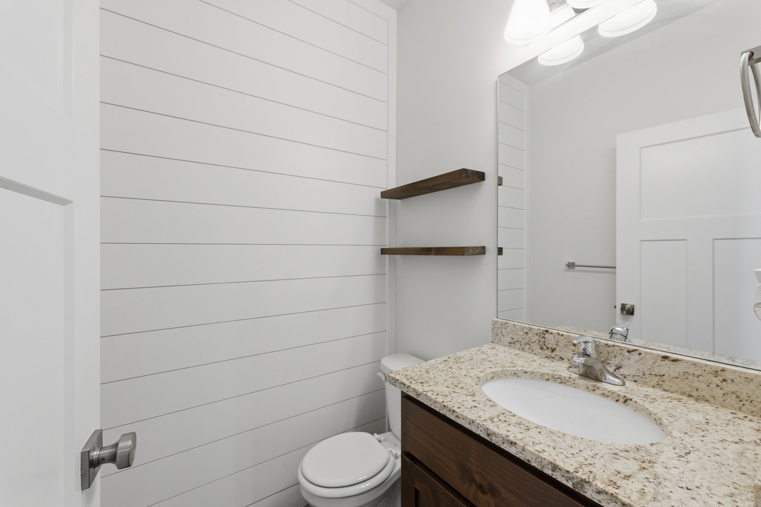 Bathroom featuring white shiplap walls, a vanity with a light-toned stone countertop, an integrated sink, and a dark wood-finish cabinet