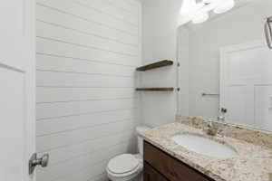 Bathroom featuring white shiplap walls, a vanity with a light-toned stone countertop, an integrated sink, and a dark wood-finish cabinet