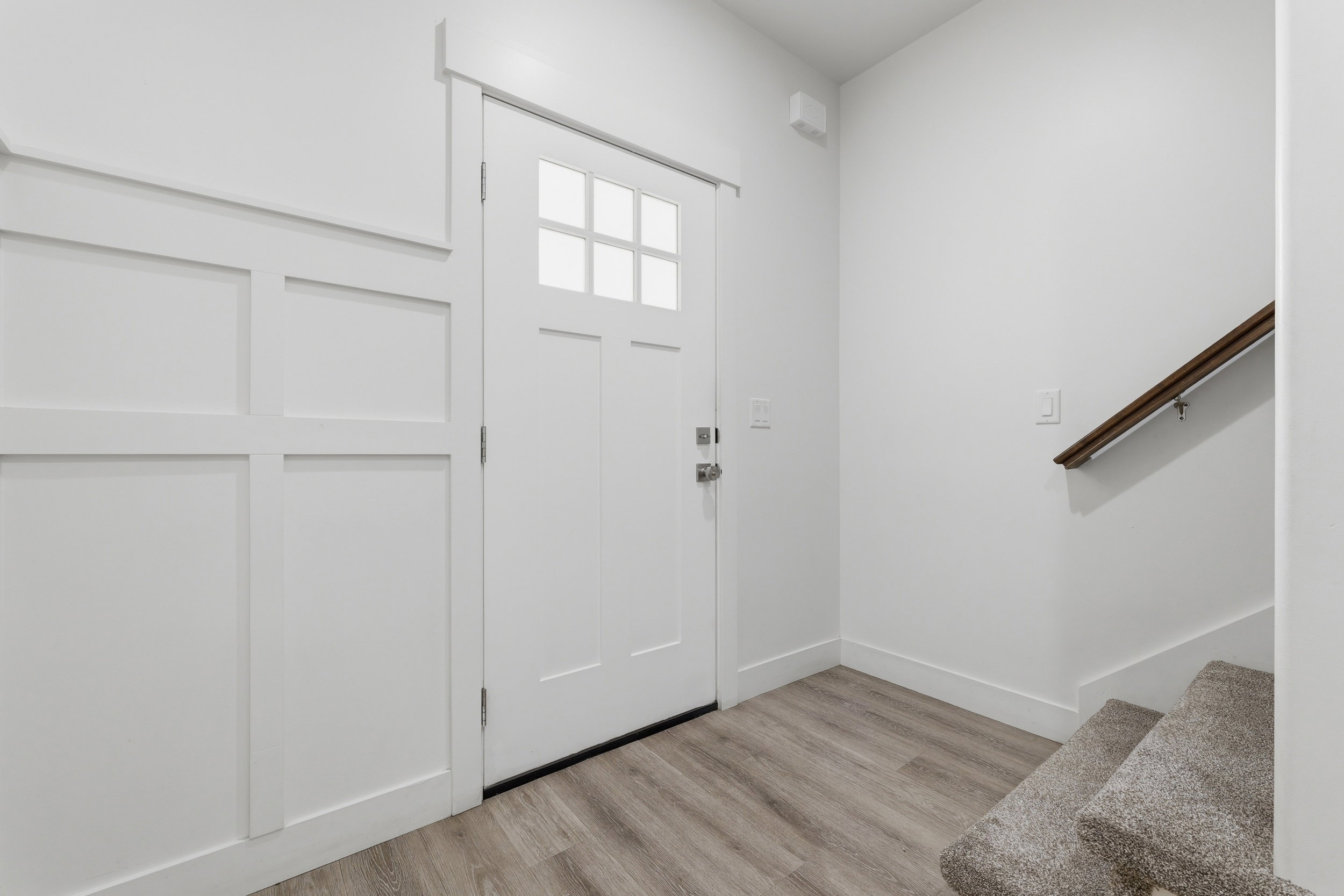 Entryway featuring a panel door with upper lites, board-and-batten wall detailing, wood-finish flooring, and a carpeted staircase with a wood handrail