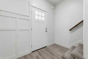 Entryway featuring a panel door with upper lites, board-and-batten wall detailing, wood-finish flooring, and a carpeted staircase with a wood handrail