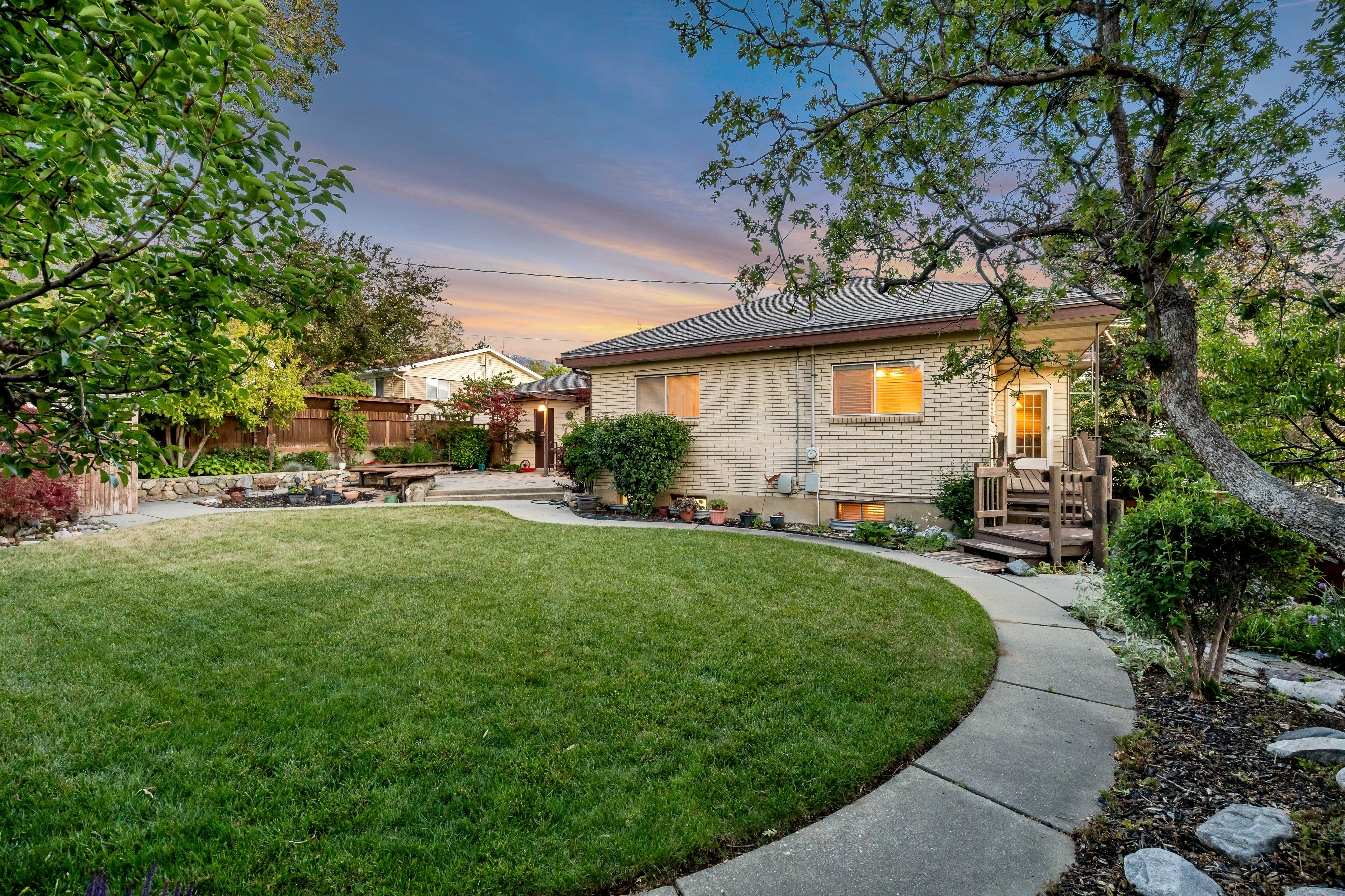 Expansive backyard featuring a manicured lawn, concrete pathway, and mature trees