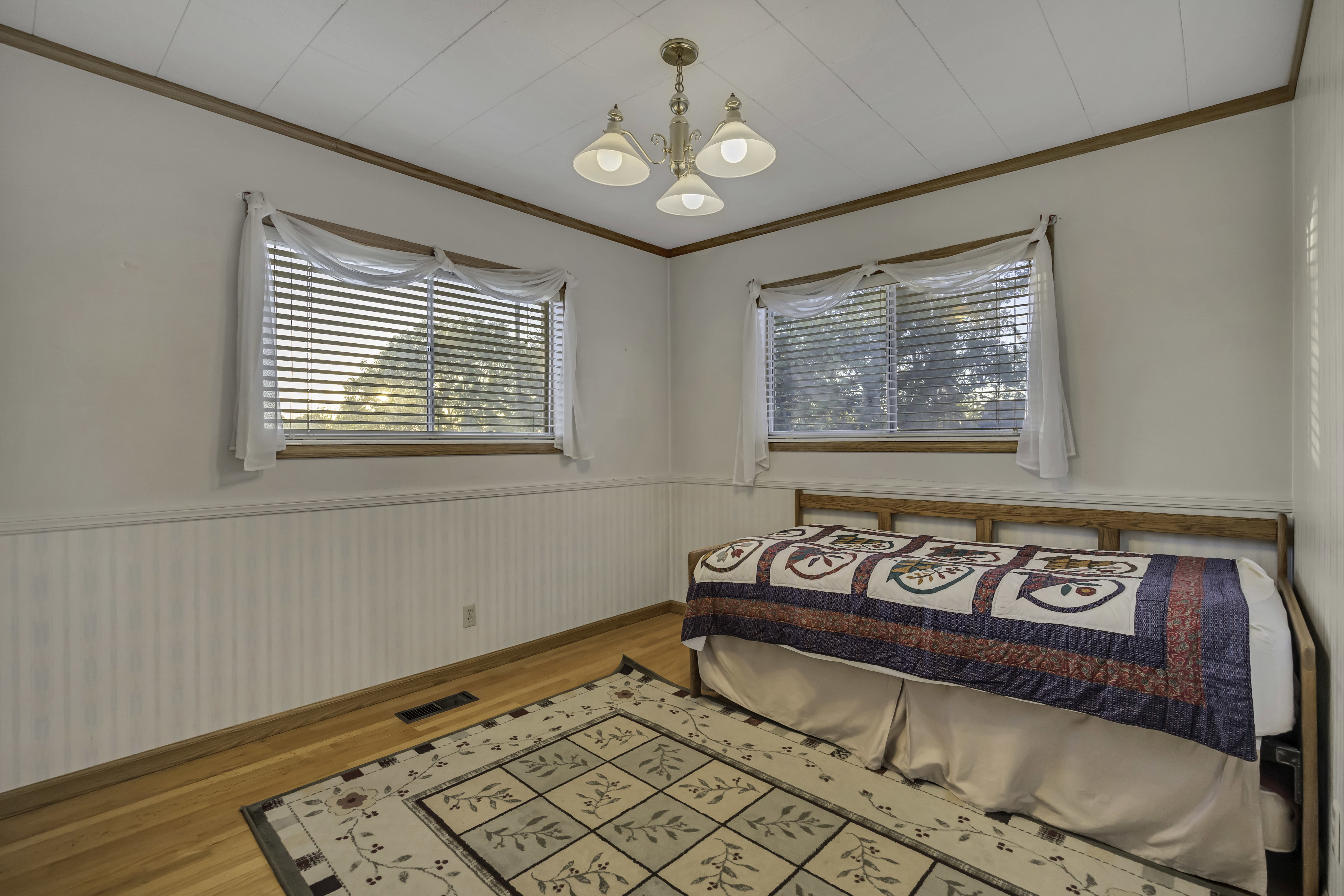 Bedroom featuring two windows with blinds, chair rail molding, and wood-finish flooring