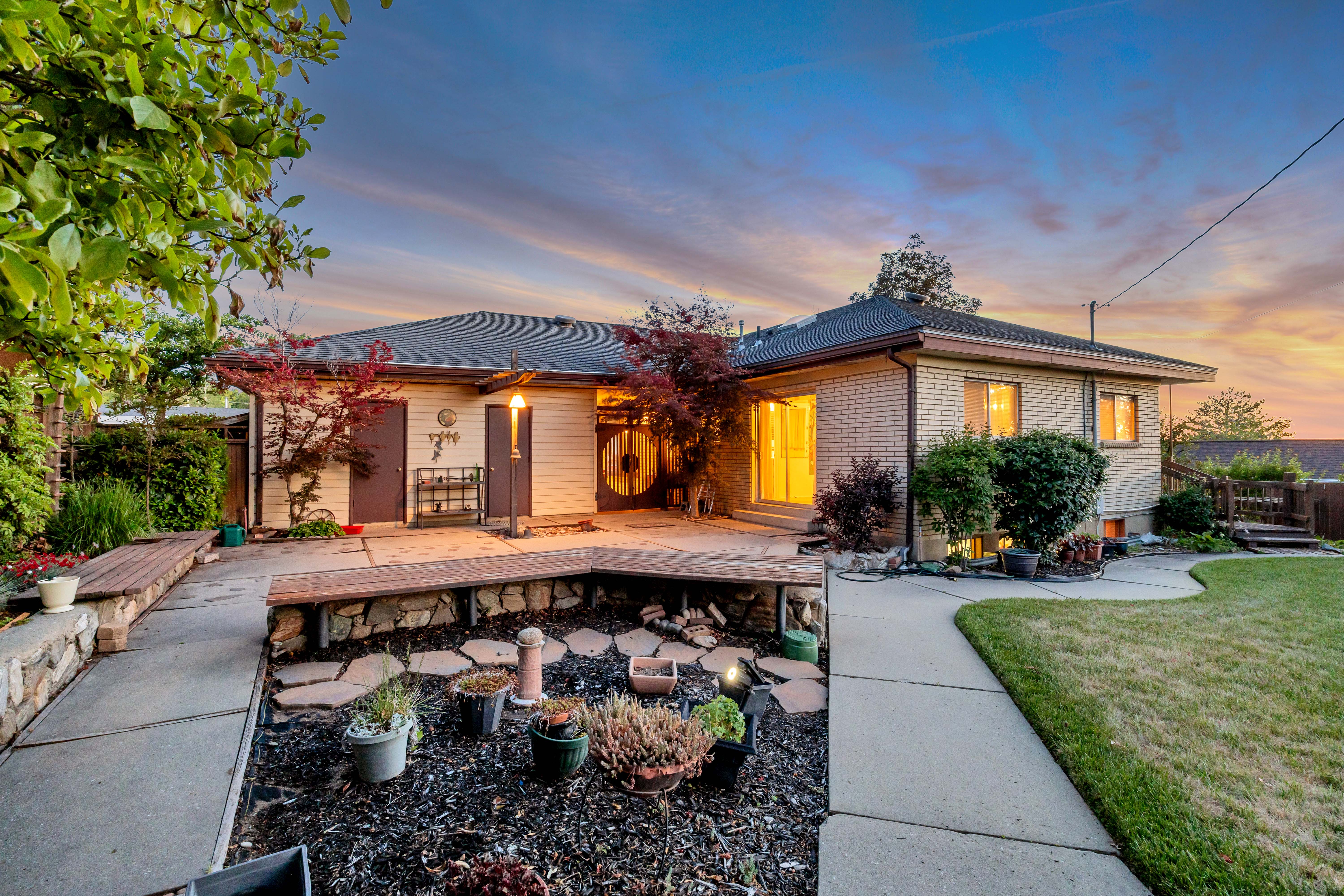 Rear exterior featuring a brick facade, private patio, built-in wooden bench seating, and an expansive lawn